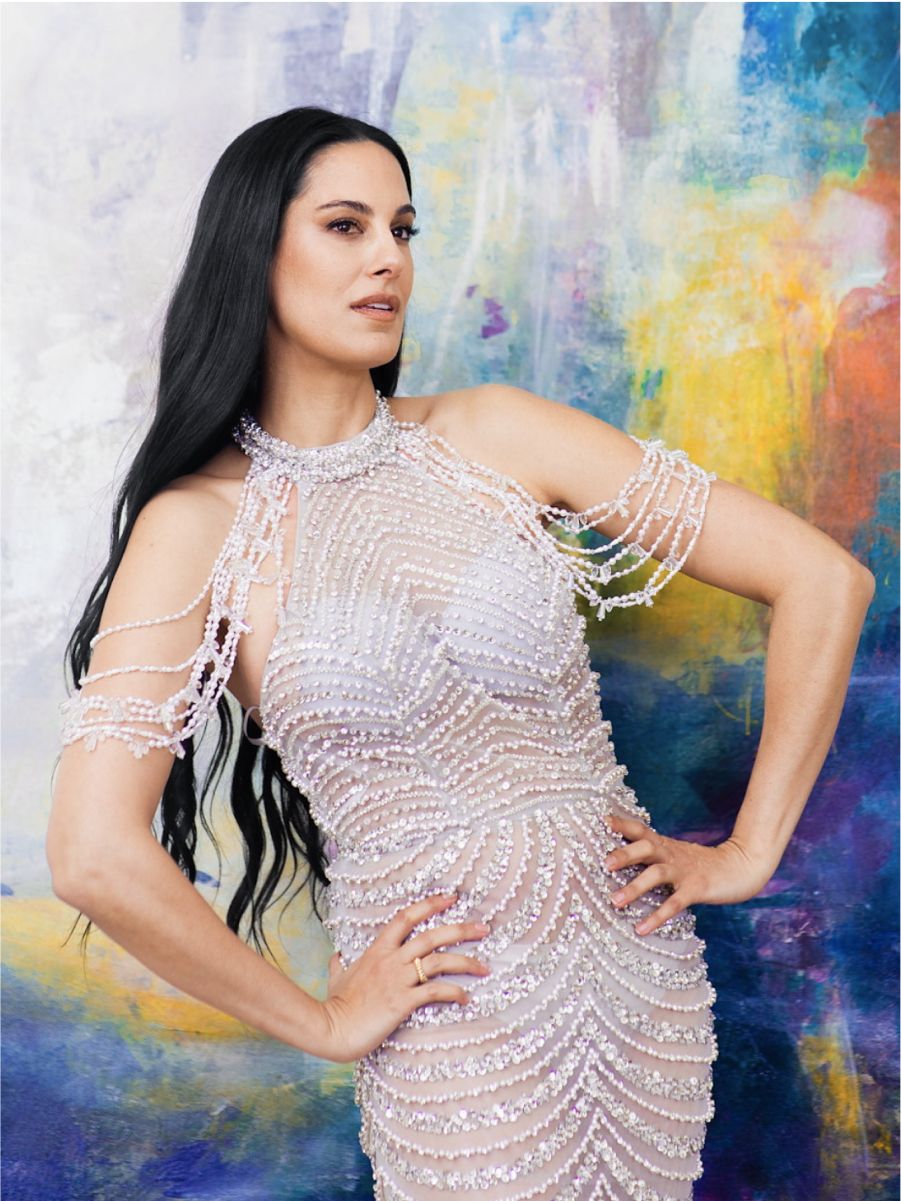 Woman in elegant beaded dress against colorful background.