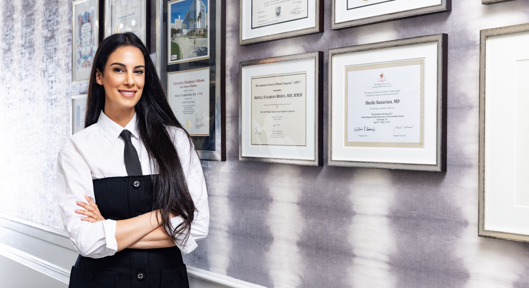 Smiling woman in front of framed certifications.
